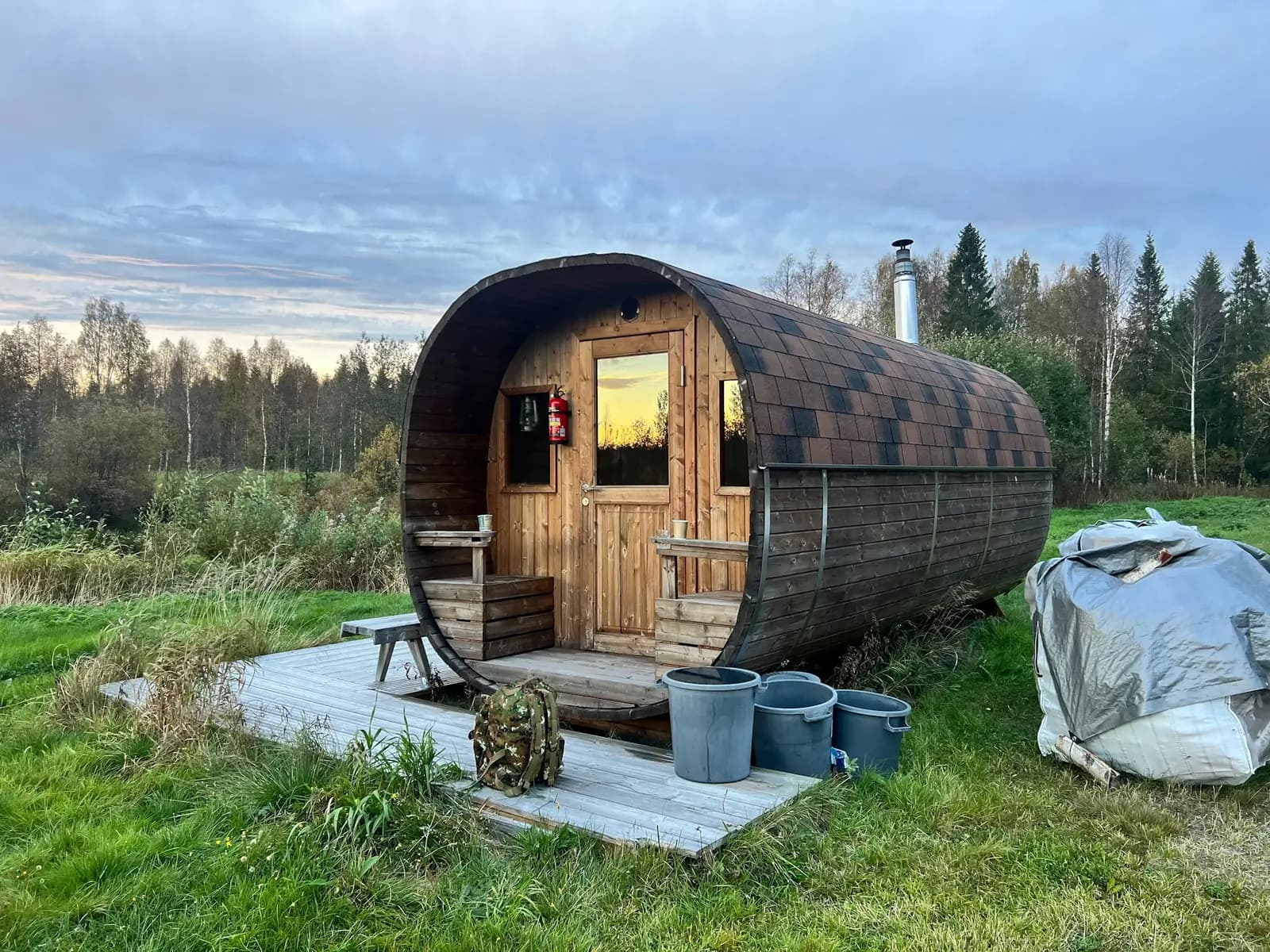 An oval wooden barrel sauna on a small deck in a grassy field