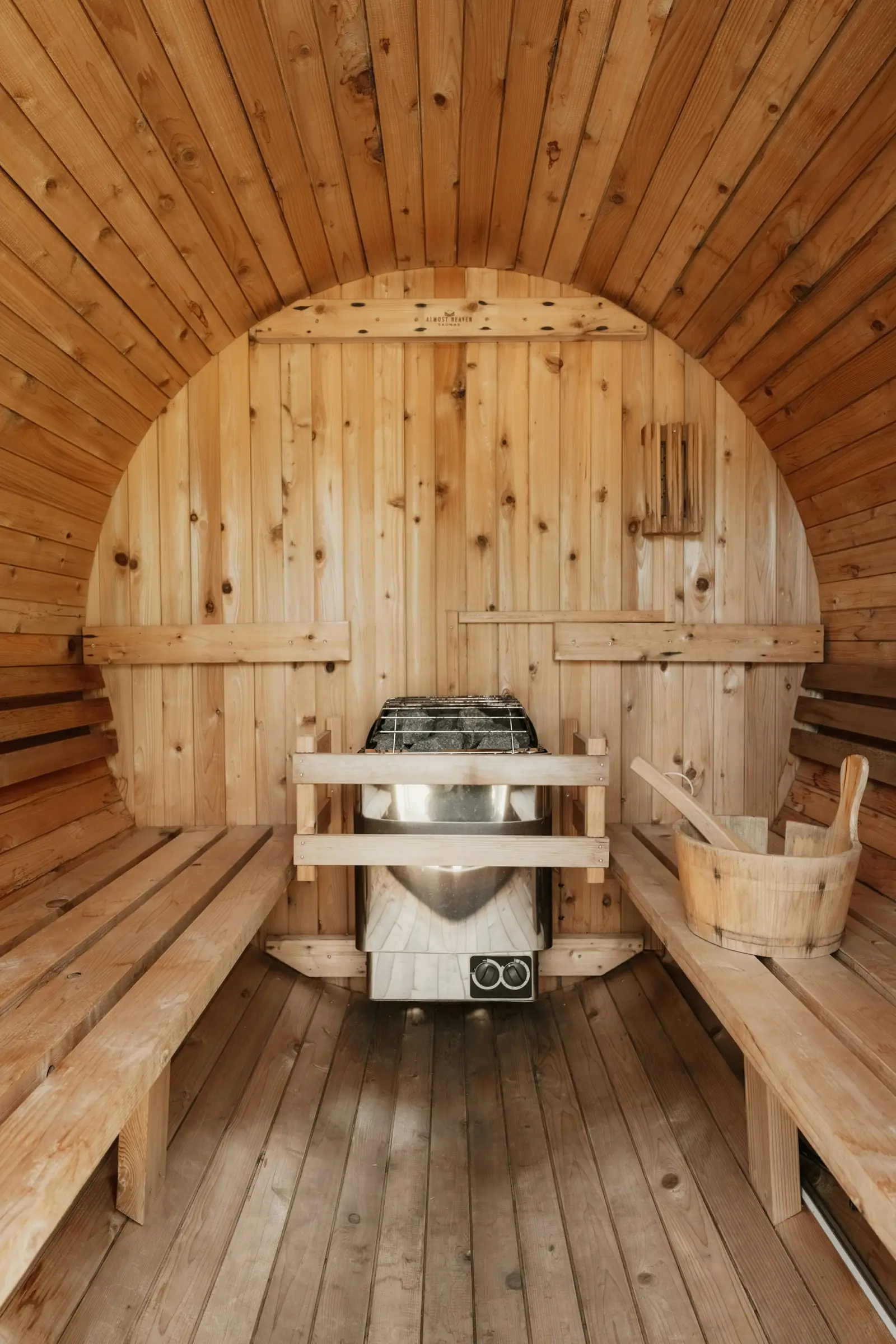 Inside a barrel sauna: curved wooden walls, benches on both sides and an electric heater at the far end