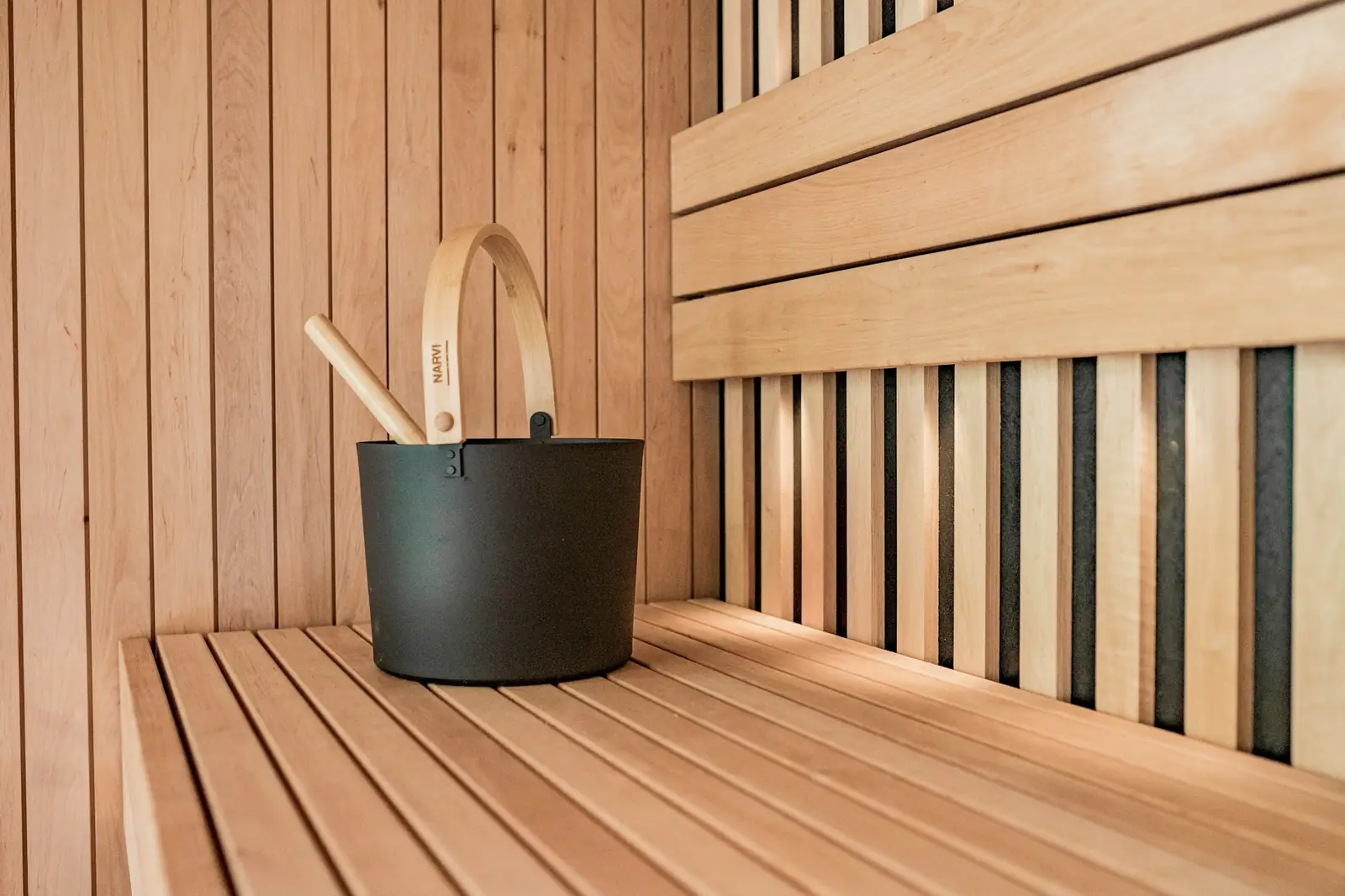 A black sauna bucket with a wooden ladle on a slatted bench