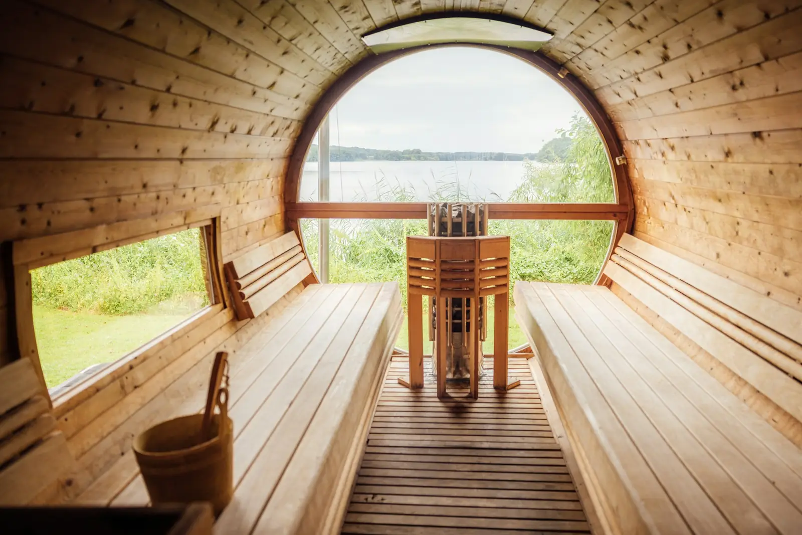 Inside a barrel sauna: benches on both sides, a heater in the middle and a round window at the far end
