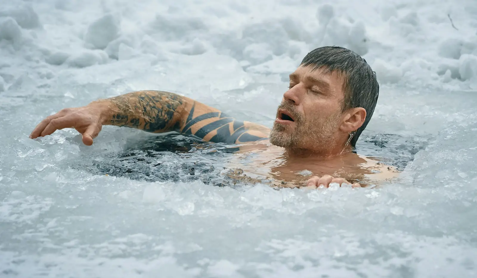 A man swimming in a hole cut in frozen water
