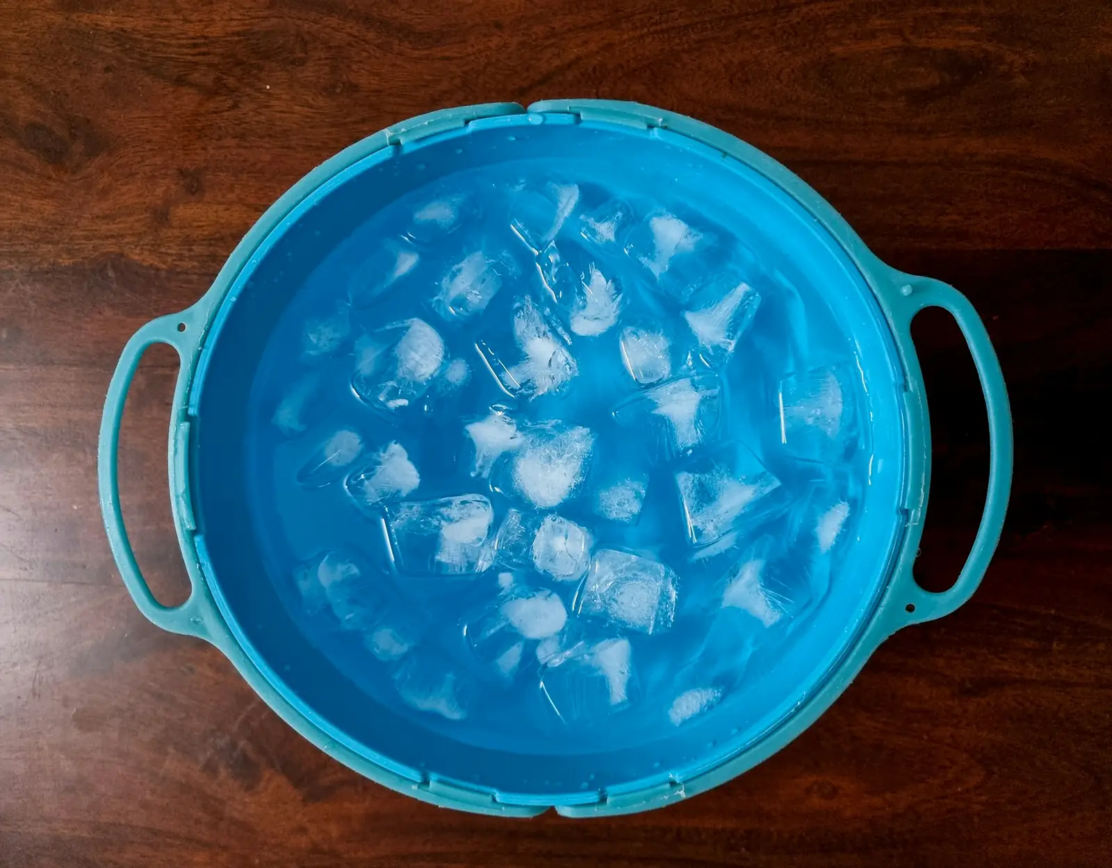 A blue tub of water and ice cubes on a wooden table, seen from above