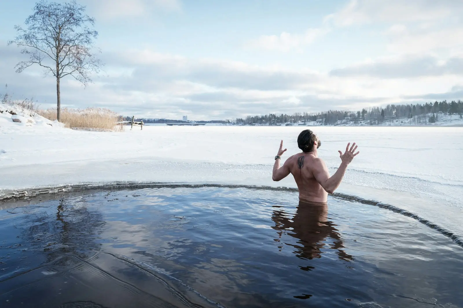 A man standing waist-deep in a hole in a frozen lake