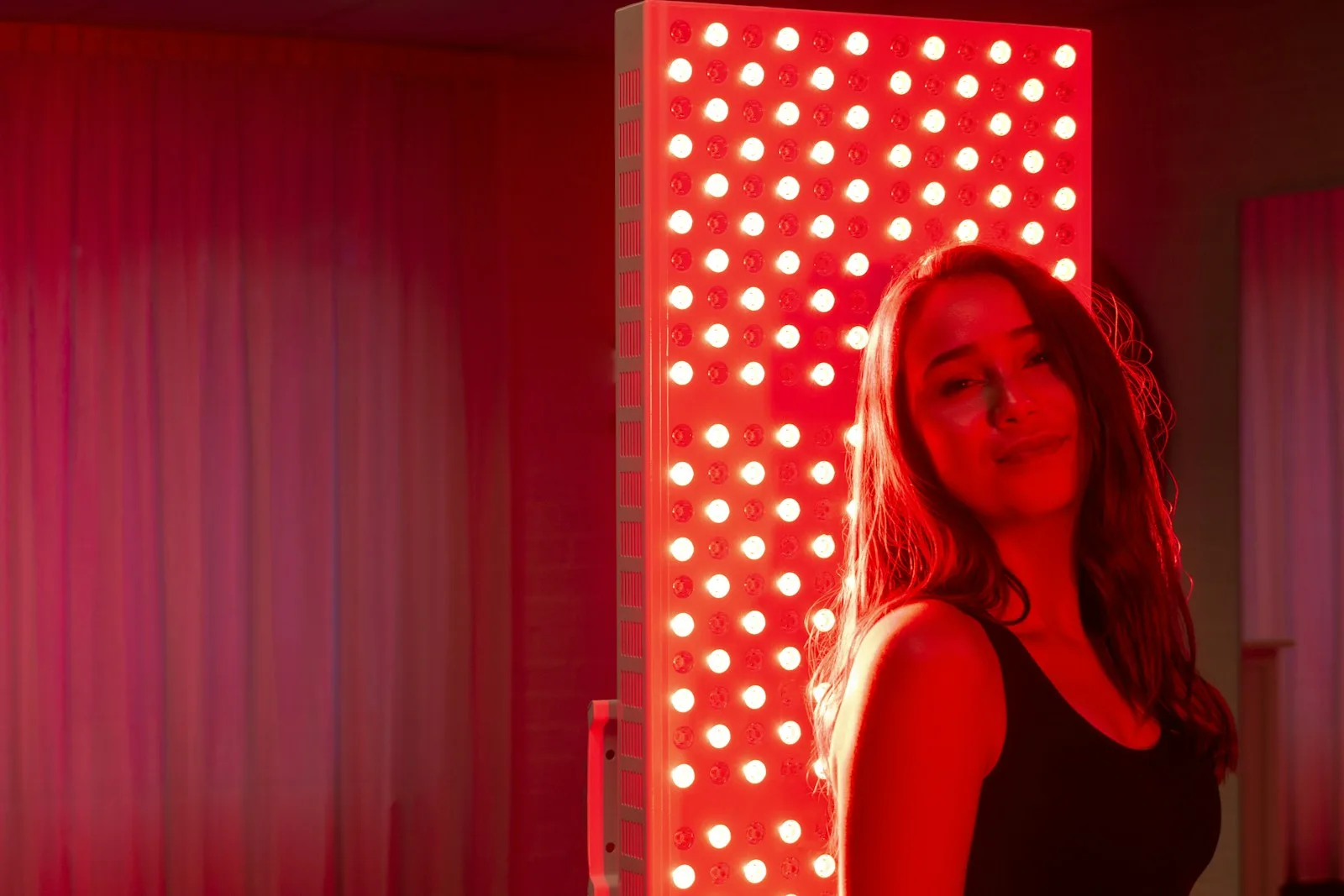 A woman in a black tank top beside a panel of bright red lights