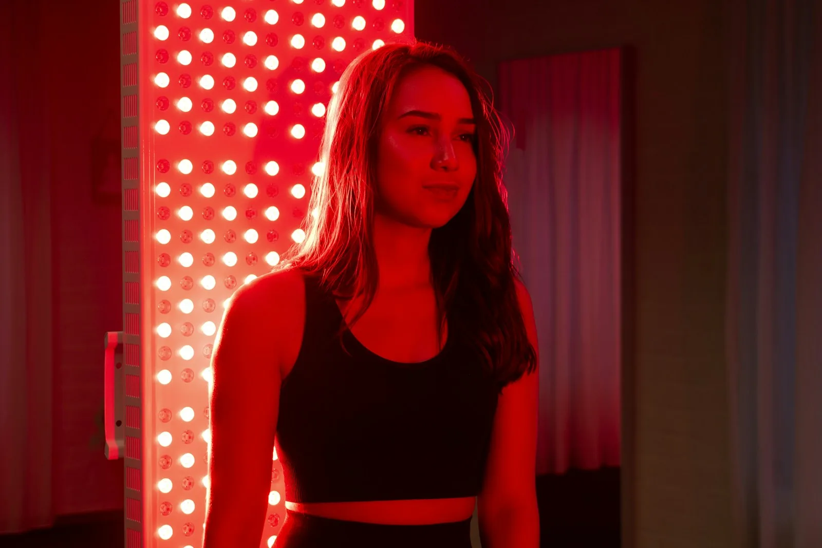 A woman standing beside a tall panel of red lights in a dark room
