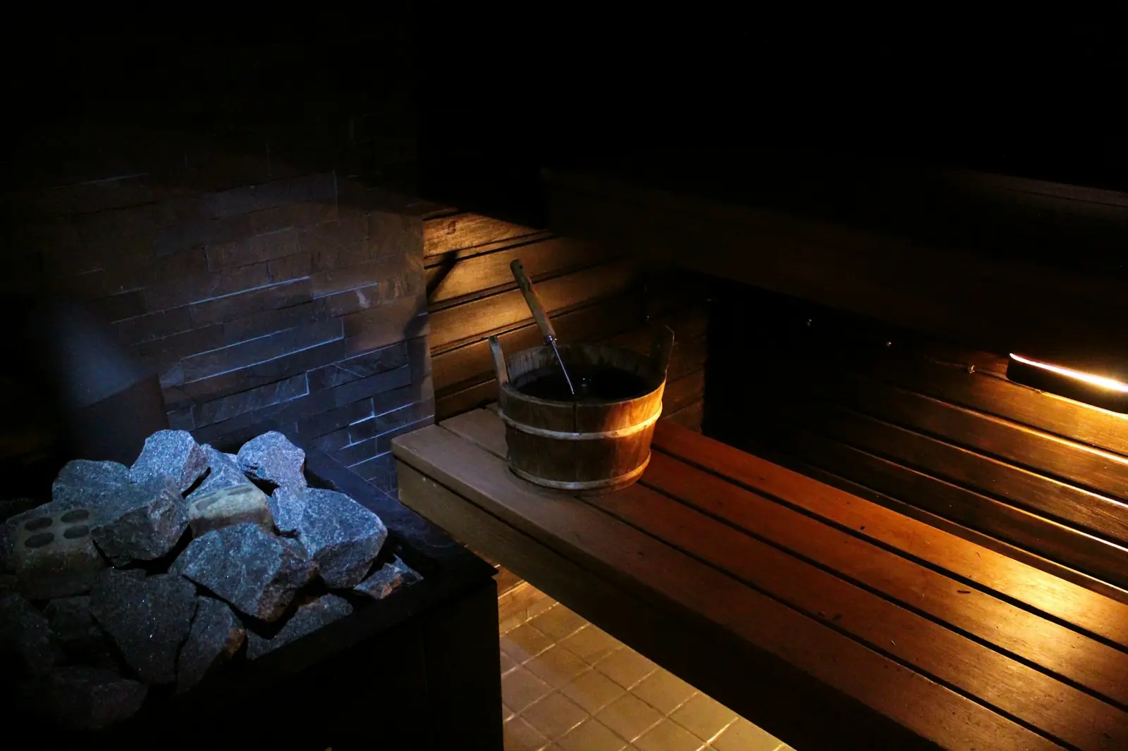 Sauna stones, a wooden bucket and a bench in a dimly lit sauna