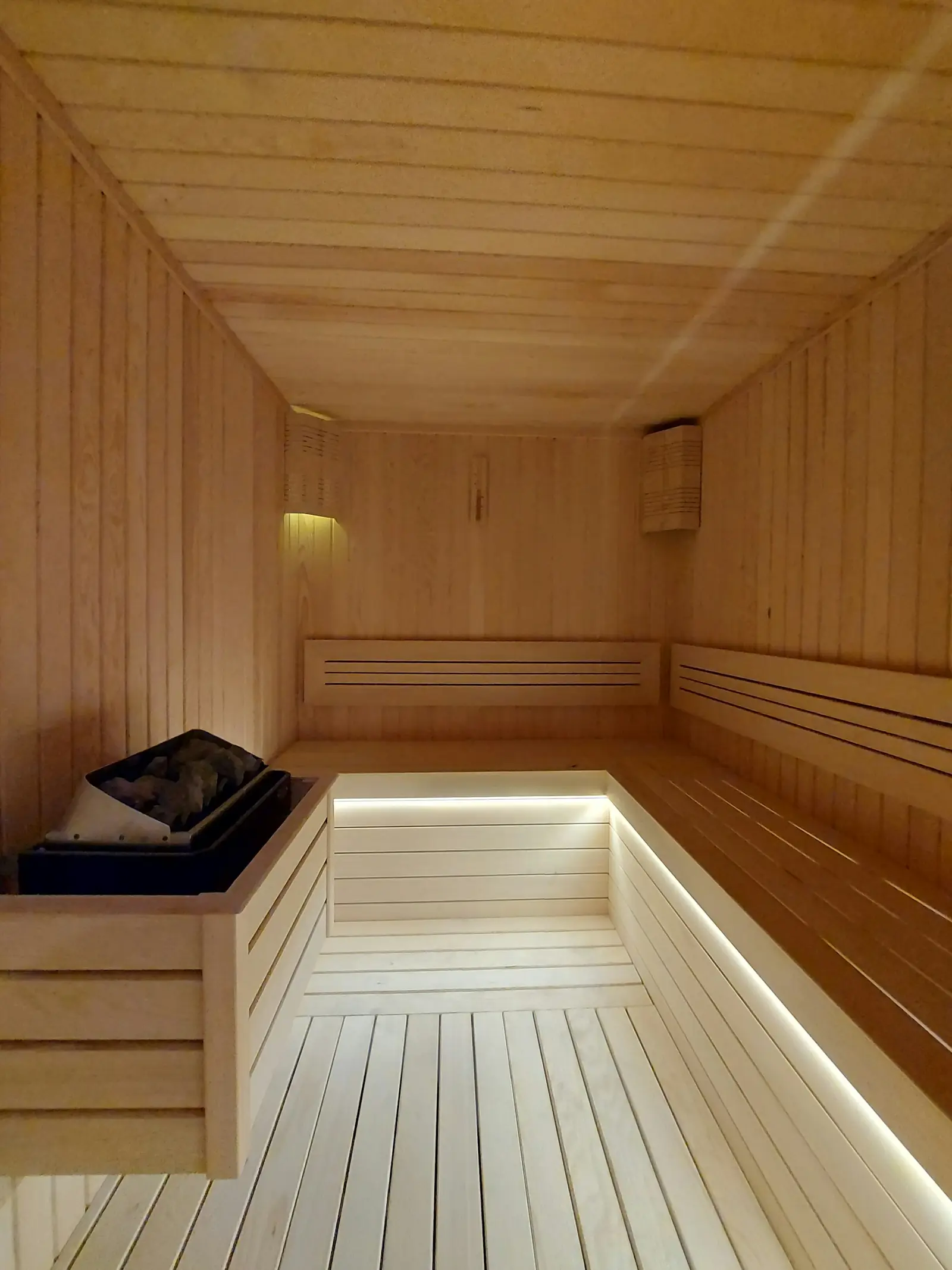 A light wood indoor sauna with an L-shaped bench and lighting under the bench