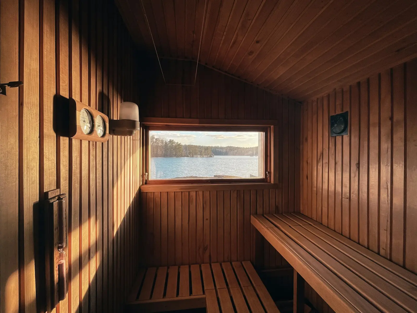A dark wooden sauna with benches and a small window looking out on water
