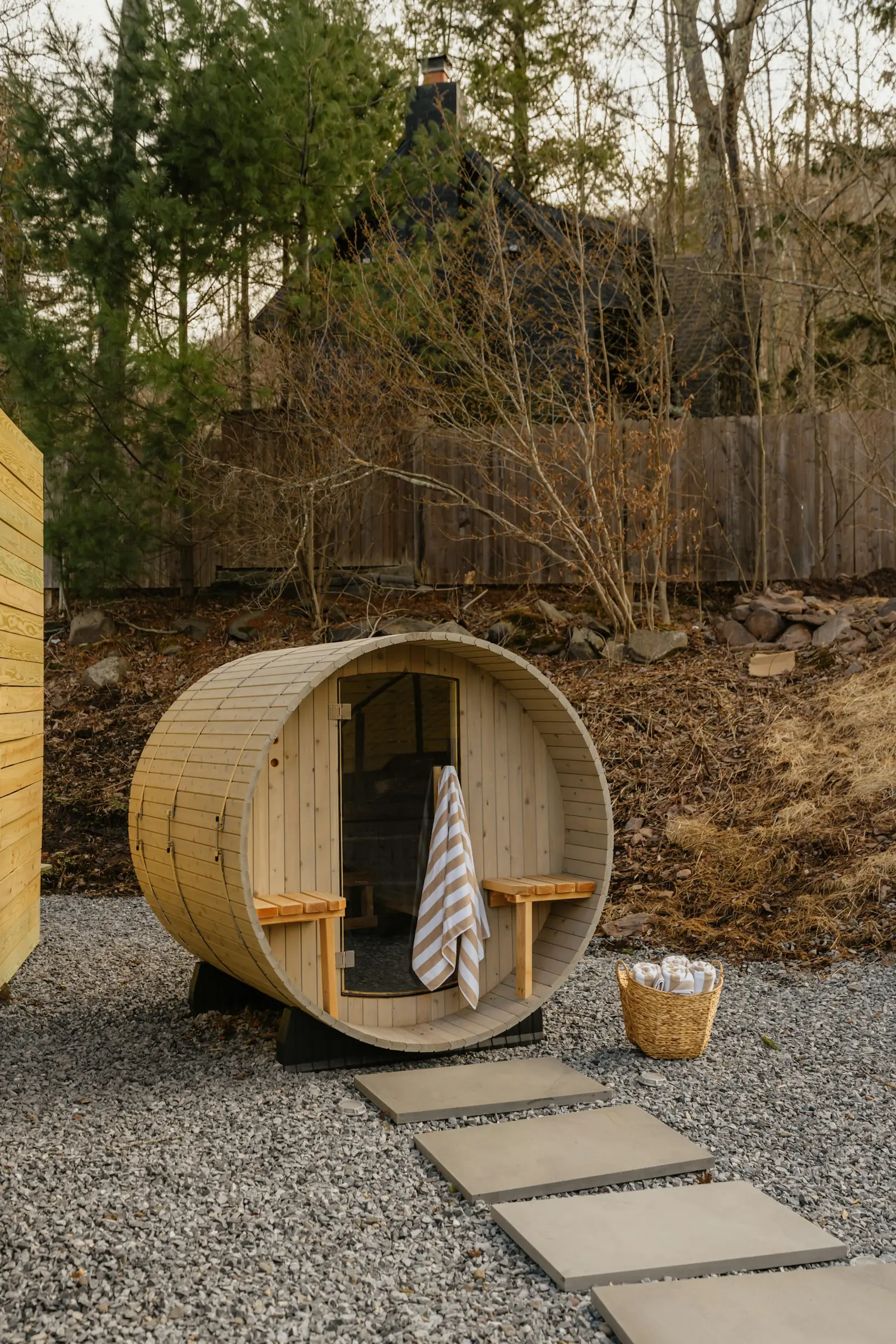 A small barrel sauna on a gravel pad with a paver path leading to the door