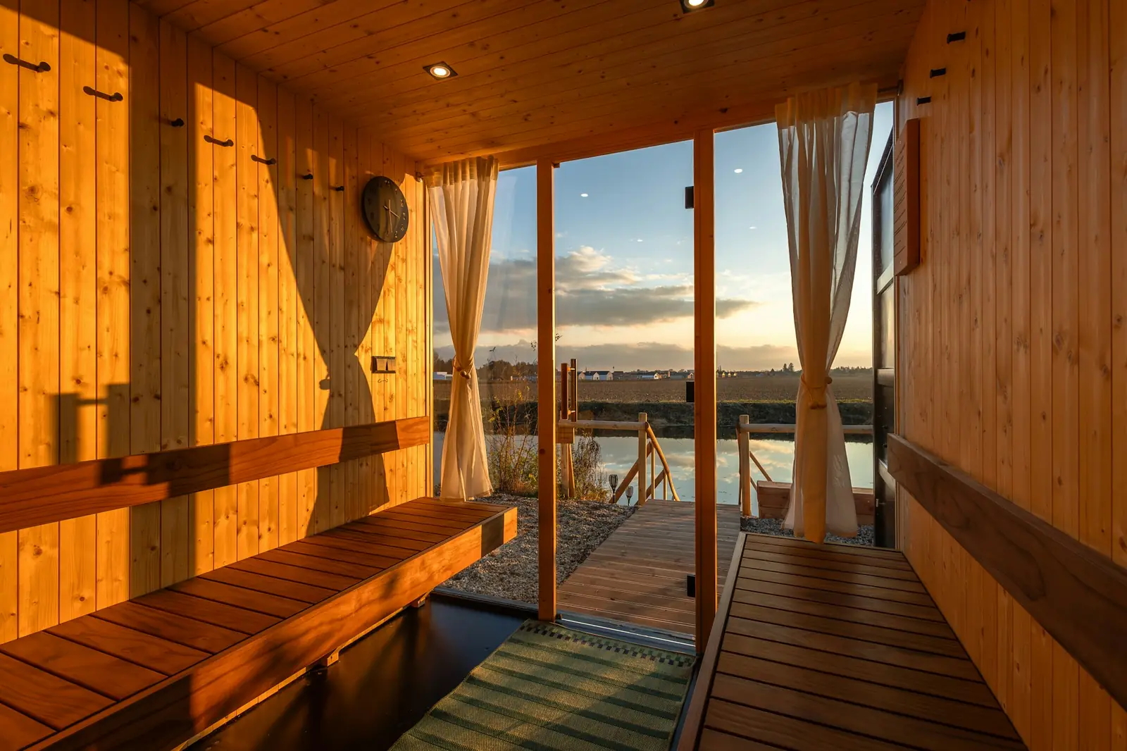 A wooden sauna room with benches and glass doors open onto a dock and water