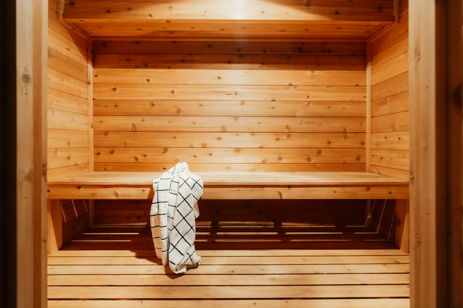 A light wood indoor sauna with two bench levels and a checked towel on the upper bench