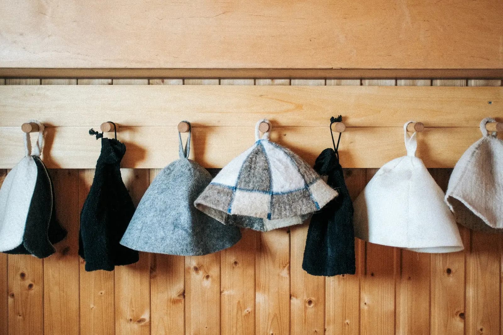Felt sauna hats hanging on hooks on a wooden wall