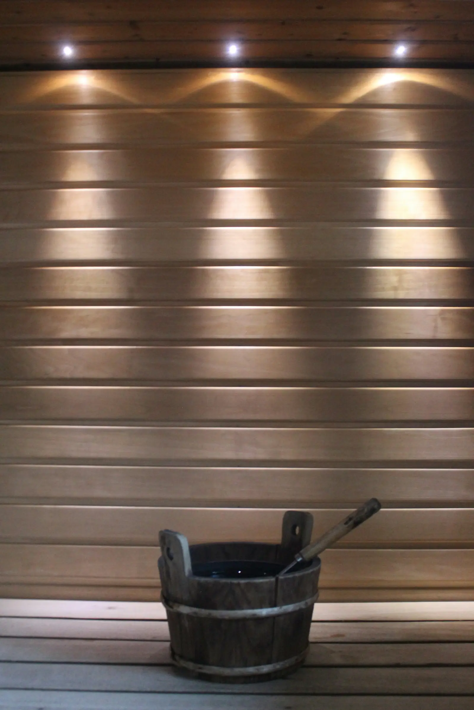 A wooden sauna bucket and ladle on a bench under small ceiling lights